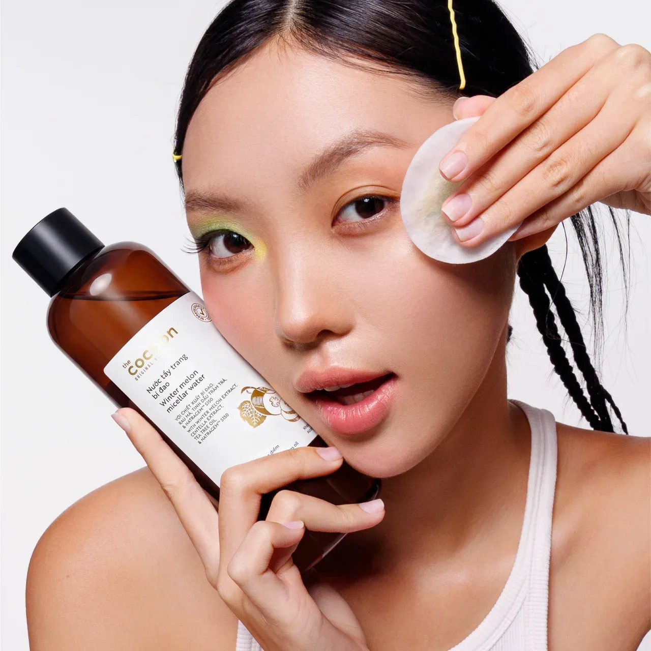 Người mẫu dùng bông tẩy trang bên cạnh chai nước tẩy trang bí đao Cocoon